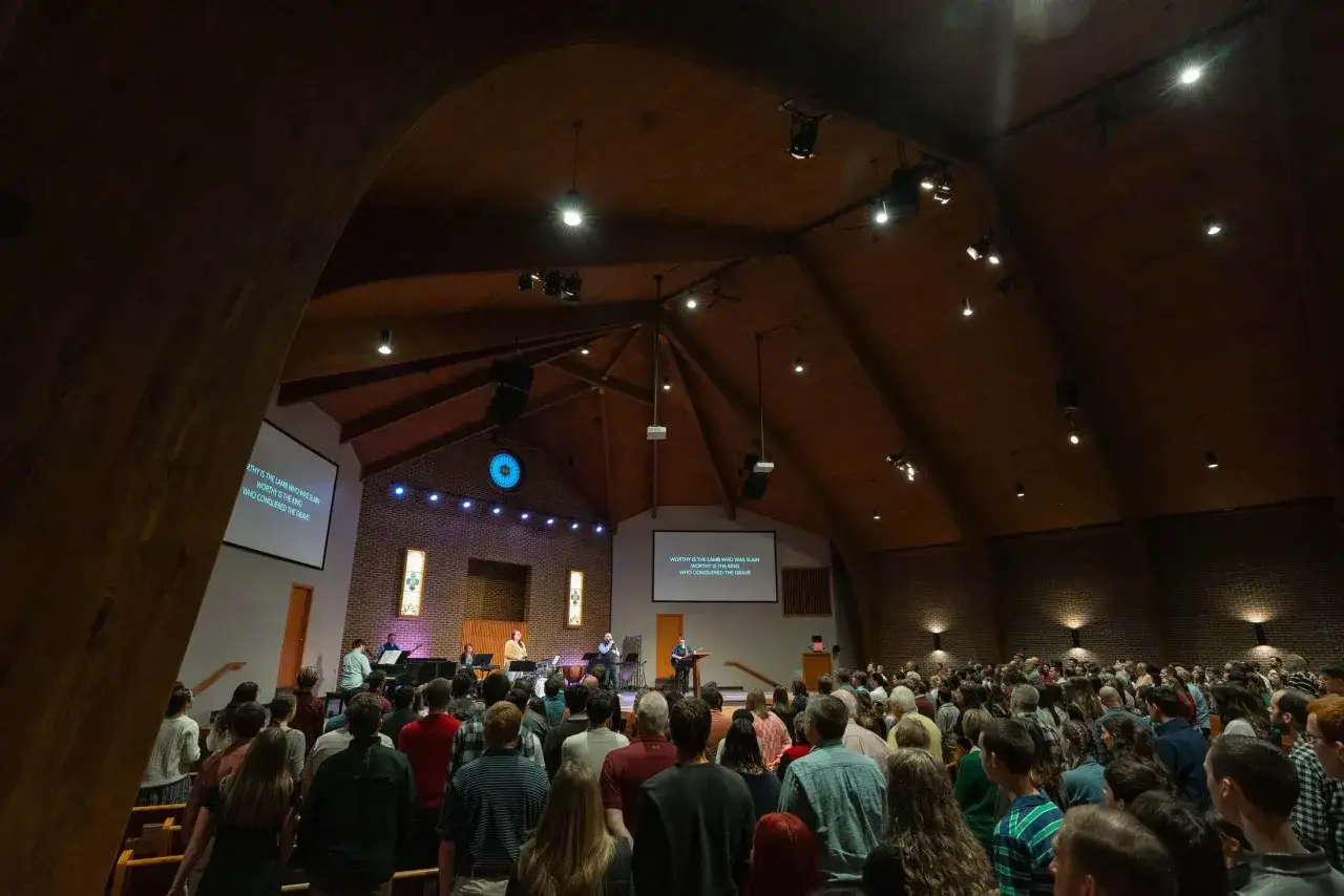 A congregation gathers in a modern Baptist church, singing along to lyrics displayed on a screen.