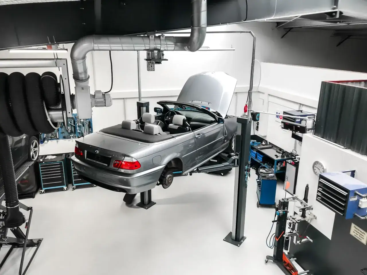 Silberner BMW Cabrio auf Hebebühne in Werkstatt. Werkzeuge und Ersatzteile deuten auf anstehende BMW Service Kosten hin.