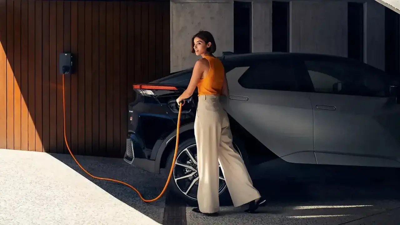 Kobieta podłącza do ładowania nowoczesną Toyotę plug-in. Pomarańczowy kabel tworzy dynamiczną linię.