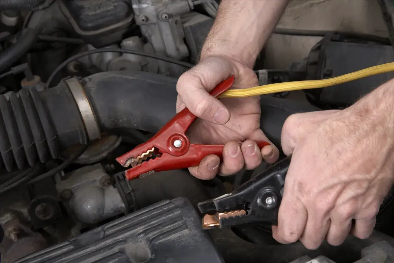 H&auml;nde verbinden Starthilfekabel mit dem Minuspol der Autobatterie, um dem Motor wieder Leben einzuhauchen.
