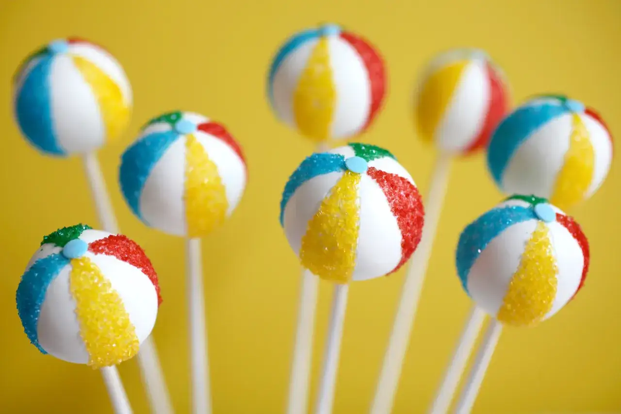 Bunte Kuchen am Stiel, die wie Beachballs aussehen, mit Zuckerstreuseln in Rot, Blau und Gelb.