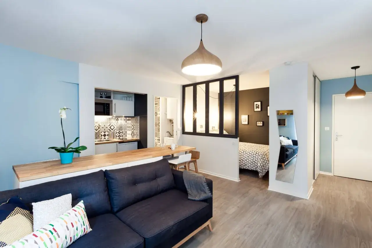 Aménagement studio 30m2 : salon cosy, cuisine moderne, chambre séparée par verrière, et coin repas.