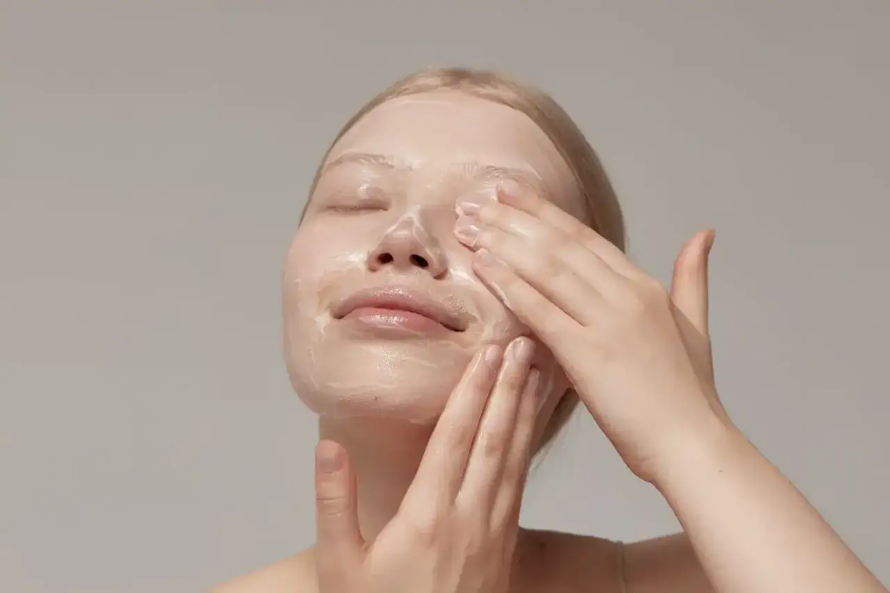 Kobieta z zamkniętymi oczami delikatnie wmasowuje krem w skórę twarzy. To idealny moment, by dowiedzieć się, jak stosować retinol dla najlepszych efektów.