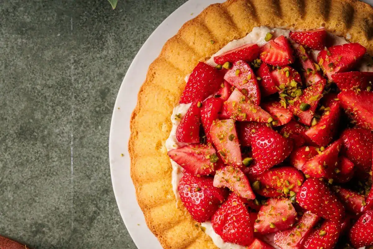 Ein k&ouml;stlicher Erdbeerkuchen mit cremigem Vanillepudding und frischen Erdbeeren, bestreut mit gehackten Pistazien.
