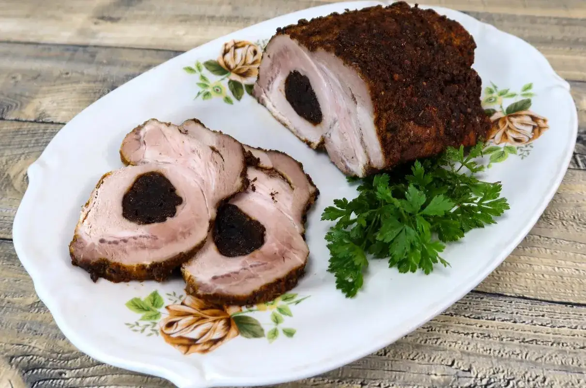 Schab pieczony ze śliwką w rękawie, soczysty i aromatyczny, pokrojony na plastry, podany z natką pietruszki na ozdobnym talerzu.
