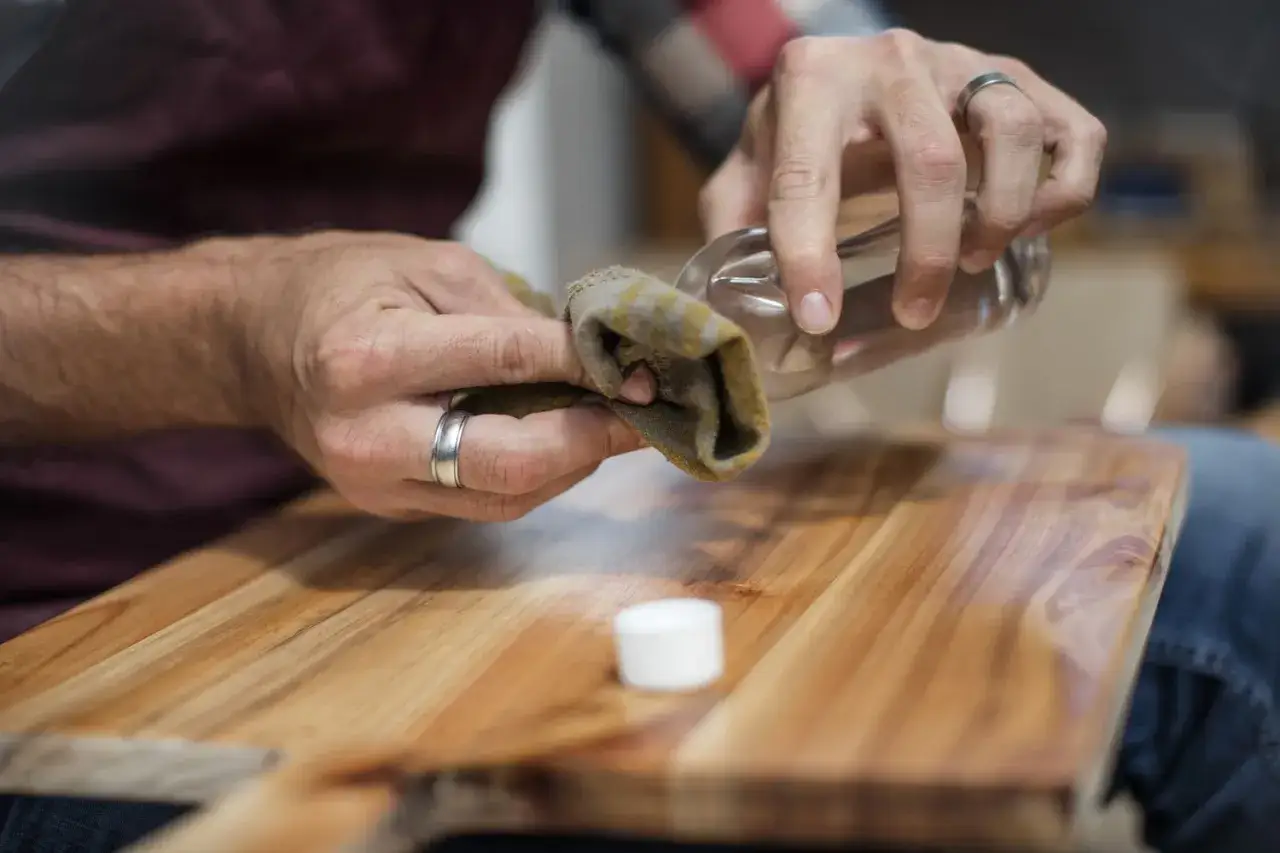 Manos aplicando aceite a una tabla de madera para nutrir madera sin barnizar.