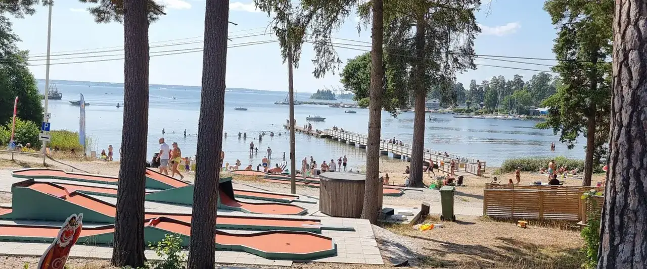 Minigolfbanor vid Engesbergs camping. Folk badar och solar vid en brygga i vattnet.