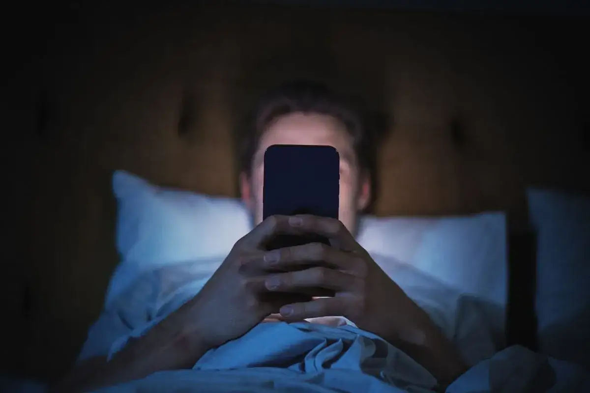 smartfon z włączonym filtrem światła niebieskiego w ciemnym pokoju