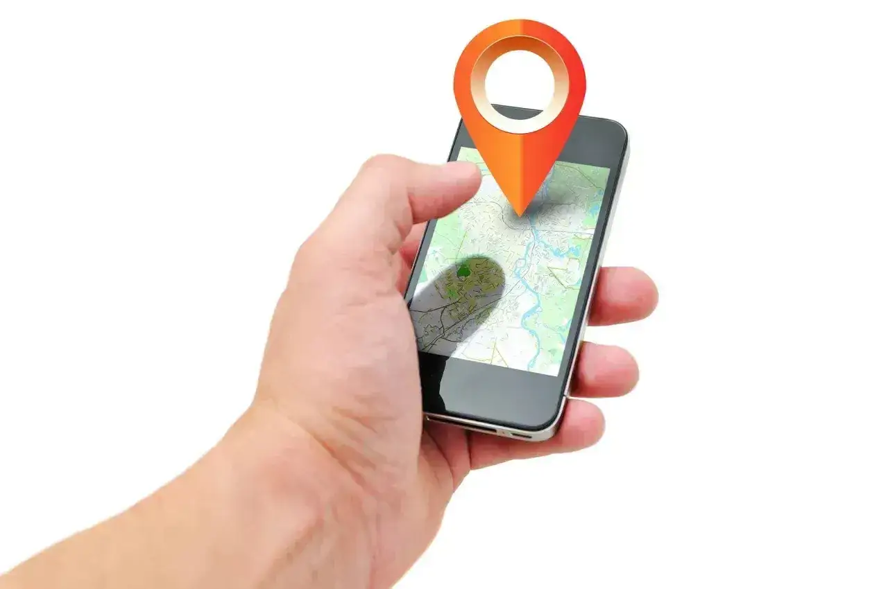 Dłoń trzyma smartfon z mapą i pinezką. Aplikacja lokalizacyjna zapewnia bezpieczna rodzina play.