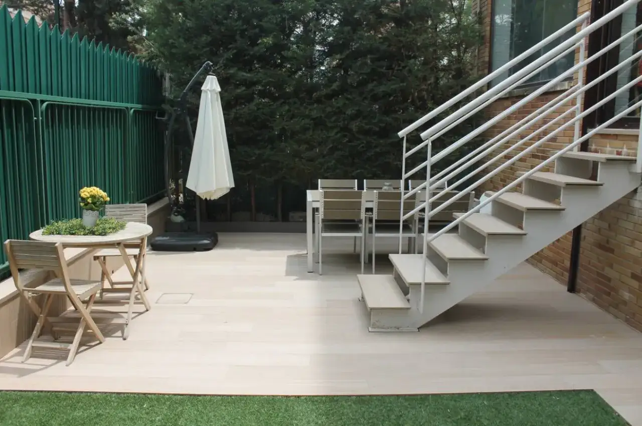 Escaleras exteriores para casas de dos pisos, con mesa y sillas de jardín, y sombrilla plegada.