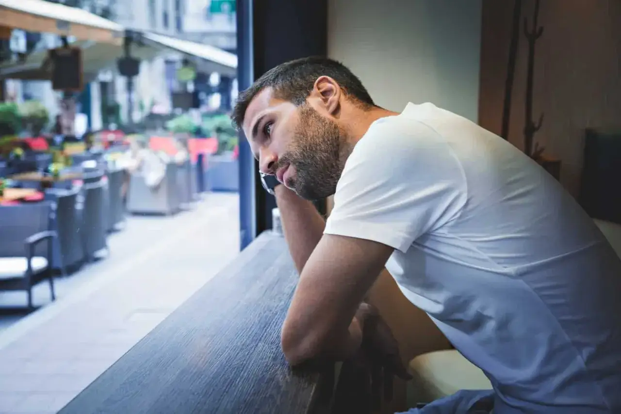 Uomo pensieroso appoggiato al bancone, con lo sguardo perso fuori dalla finestra. Sembra che voglia dire: