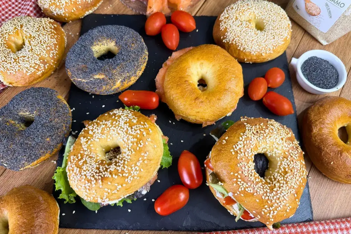 Variet&agrave; di bagel dolci e salati, alcuni con semi di sesamo, altri con semi di papavero, accompagnati da pomodorini e salmone.