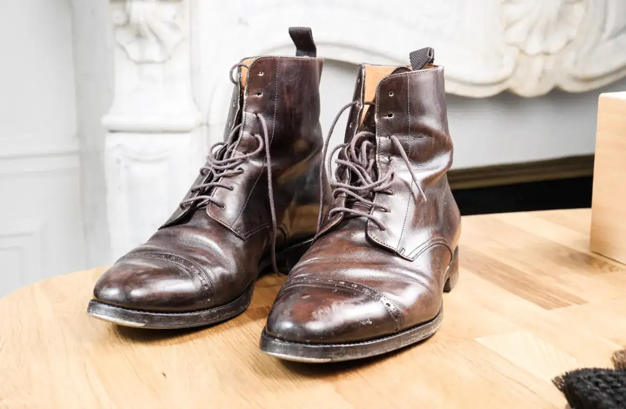 Paire de bottines en cuir griffé marron foncé, lacées, posées sur une table en bois.