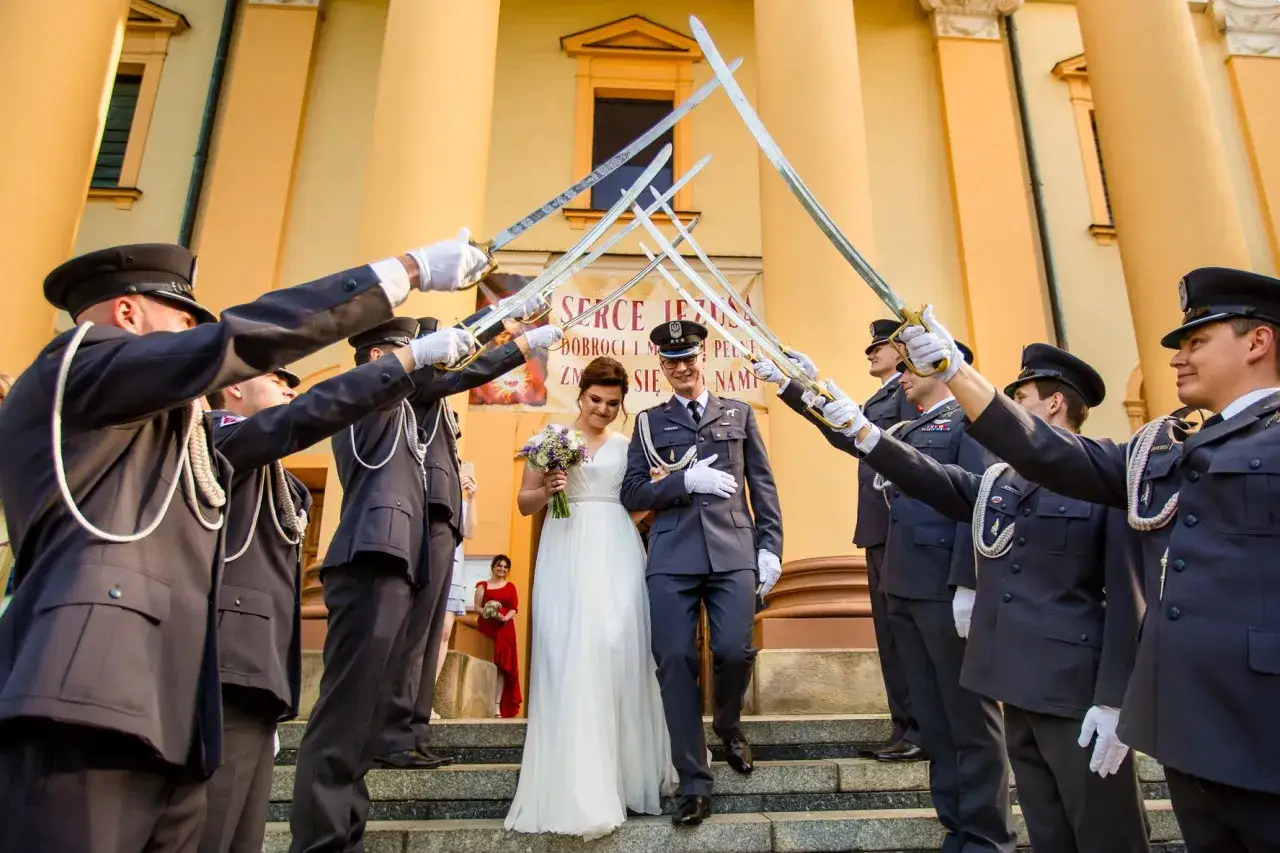 Para młoda przechodzi pod łukiem z szabel, tworząc tradycyjny marsz weselny.