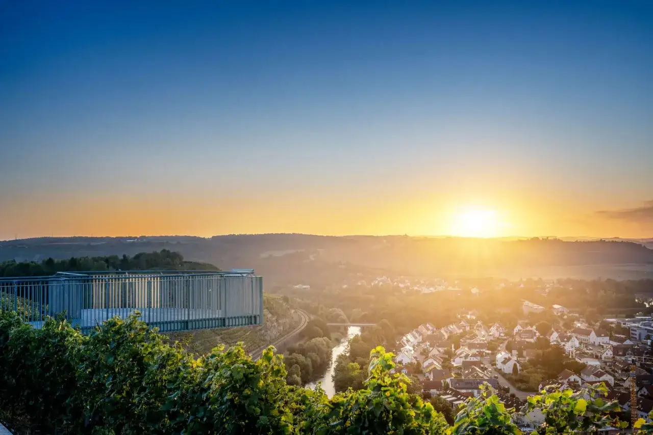 Sonnenuntergang &uuml;ber Weinbergen und einem Dorf bei Stuttgart. Eine Aussichtsplattform bietet Blick auf die Landschaft.