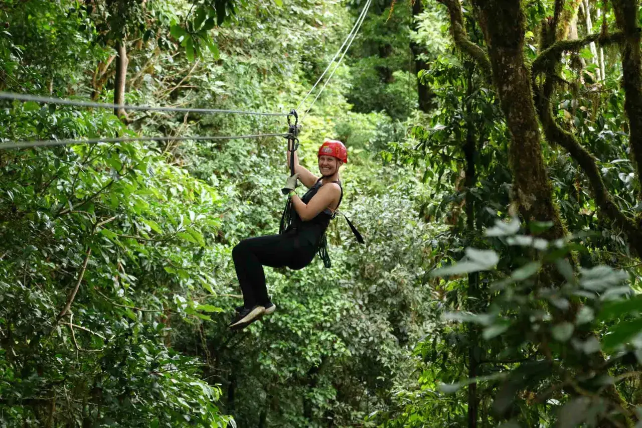 En glad kvinna åker linbana genom en frodig regnskog. Ett perfekt tips för din resa till Costa Rica för äventyr!