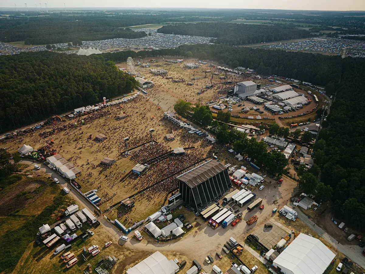 Gro&szlig;er **Hurricane Zeltplatz** mit tausenden Besuchern, B&uuml;hnen und Zelten, umgeben von Wald.