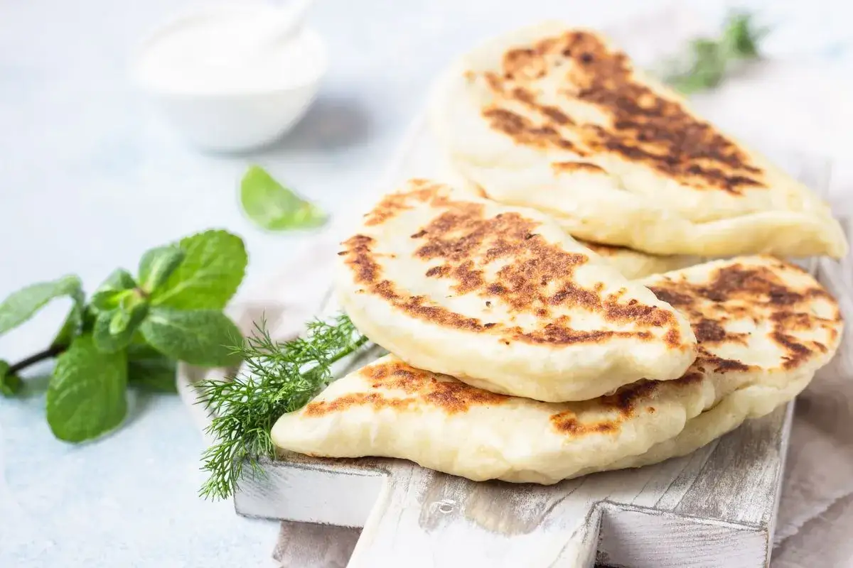 Delizioso pane in padella dorato, servito con erbe fresche e una ciotola di salsa cremosa.