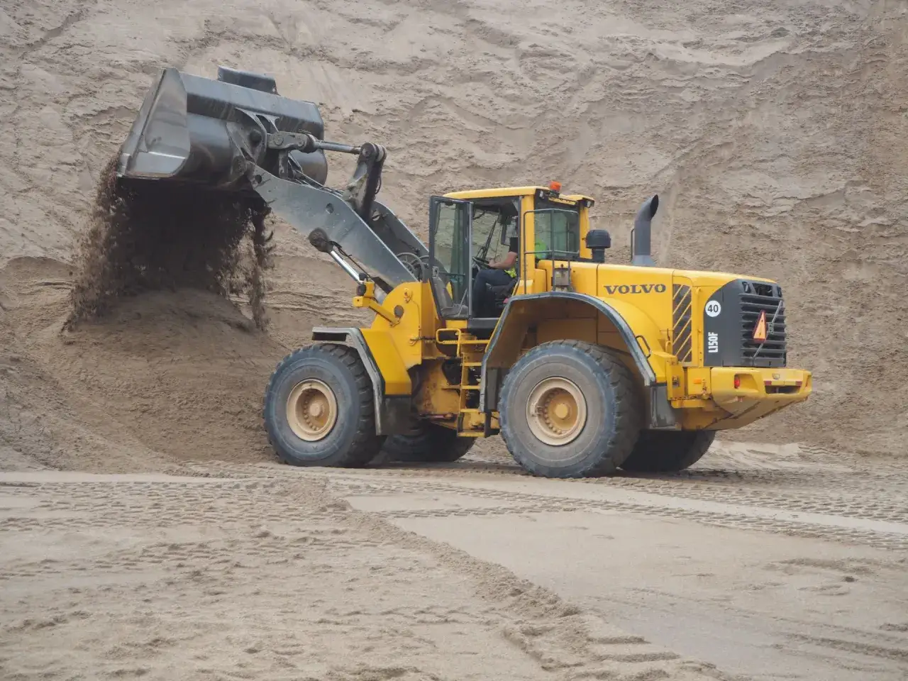 Żółta ładowarka Volvo L150F pracuje na placu budowy, przesypując piasek. Sprawdź kurs ładowarki klasa 1 cena!