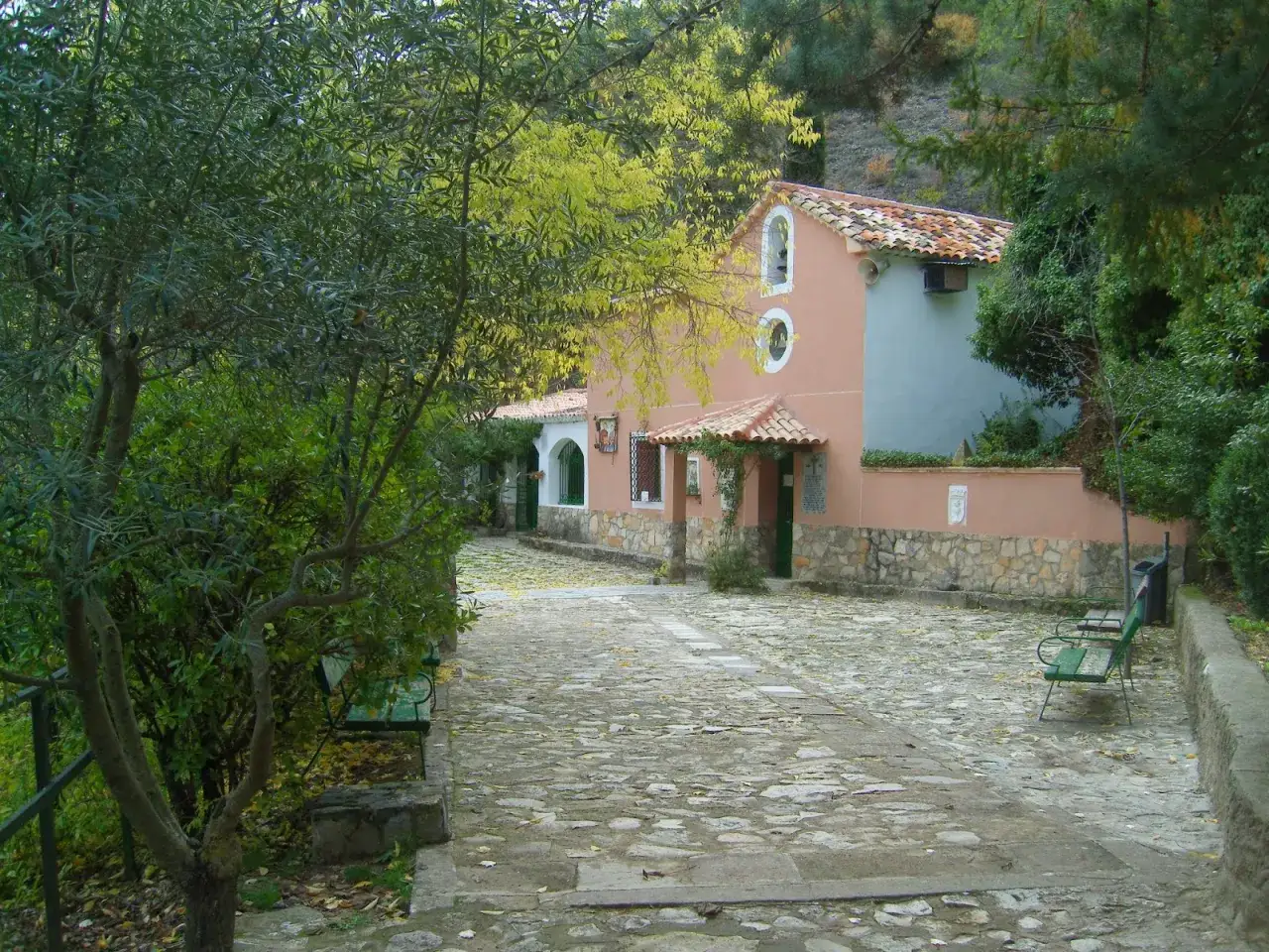 Un camino empedrado en la ruta San Juli&aacute;n el Tranquilo, Cuenca, lleva a una casa de color salm&oacute;n con detalles en piedra y un tejado de tejas.