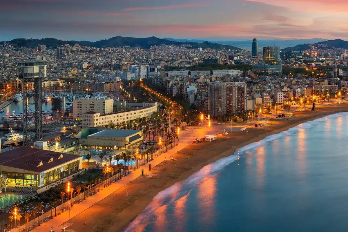 Piękne hiszpańskie miasta nad morzem, jak Barcelona, ożywają nocą. Widok na plażę, port i oświetlone budynki.