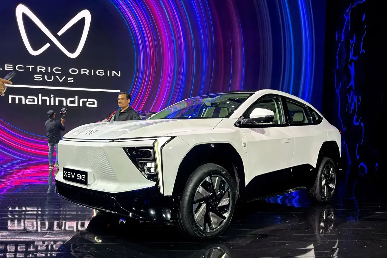 Biały SUV Mahindra XUV 9e z futurystycznym designem na tle neonowego ekranu.