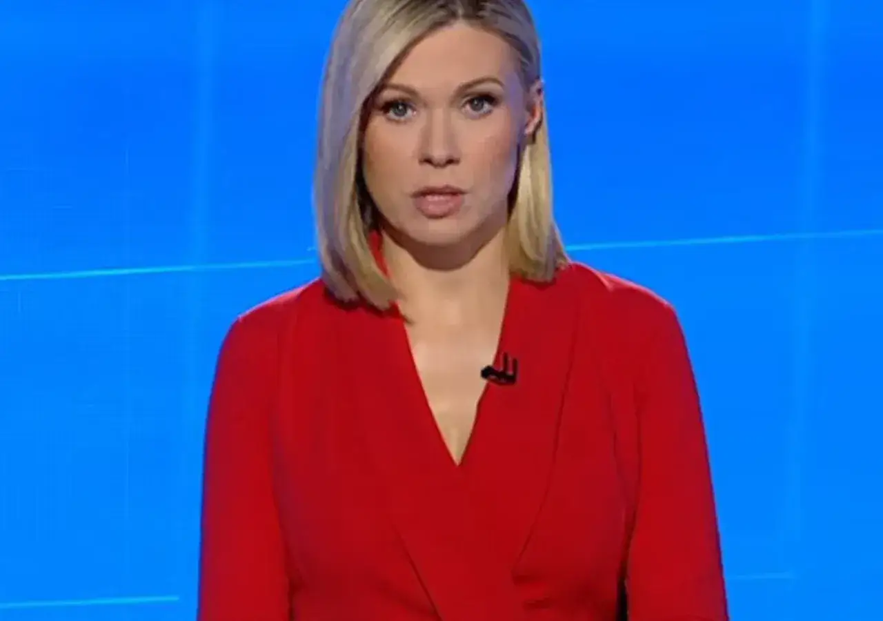 Monika Sawka w czerwonej sukience, z mężem w tle, na tle niebieskiego ekranu.