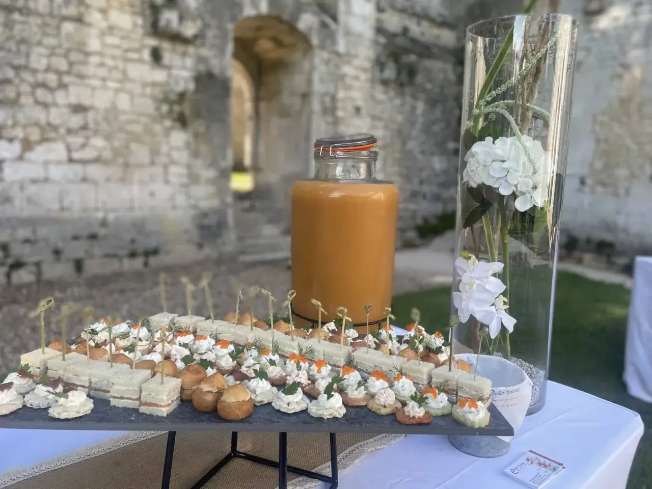 Buffet de petits fours variés, jus de fruits et fleurs blanches pour un vin d'honneur en extérieur.