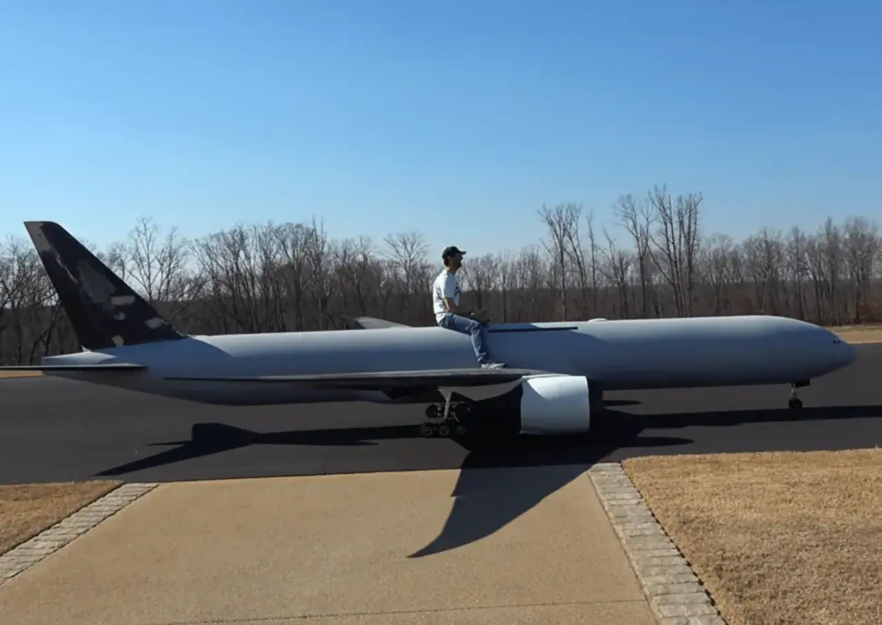 Mann sitzt auf einem riesigen ramy rc Flugzeugmodell auf einem Rollfeld.