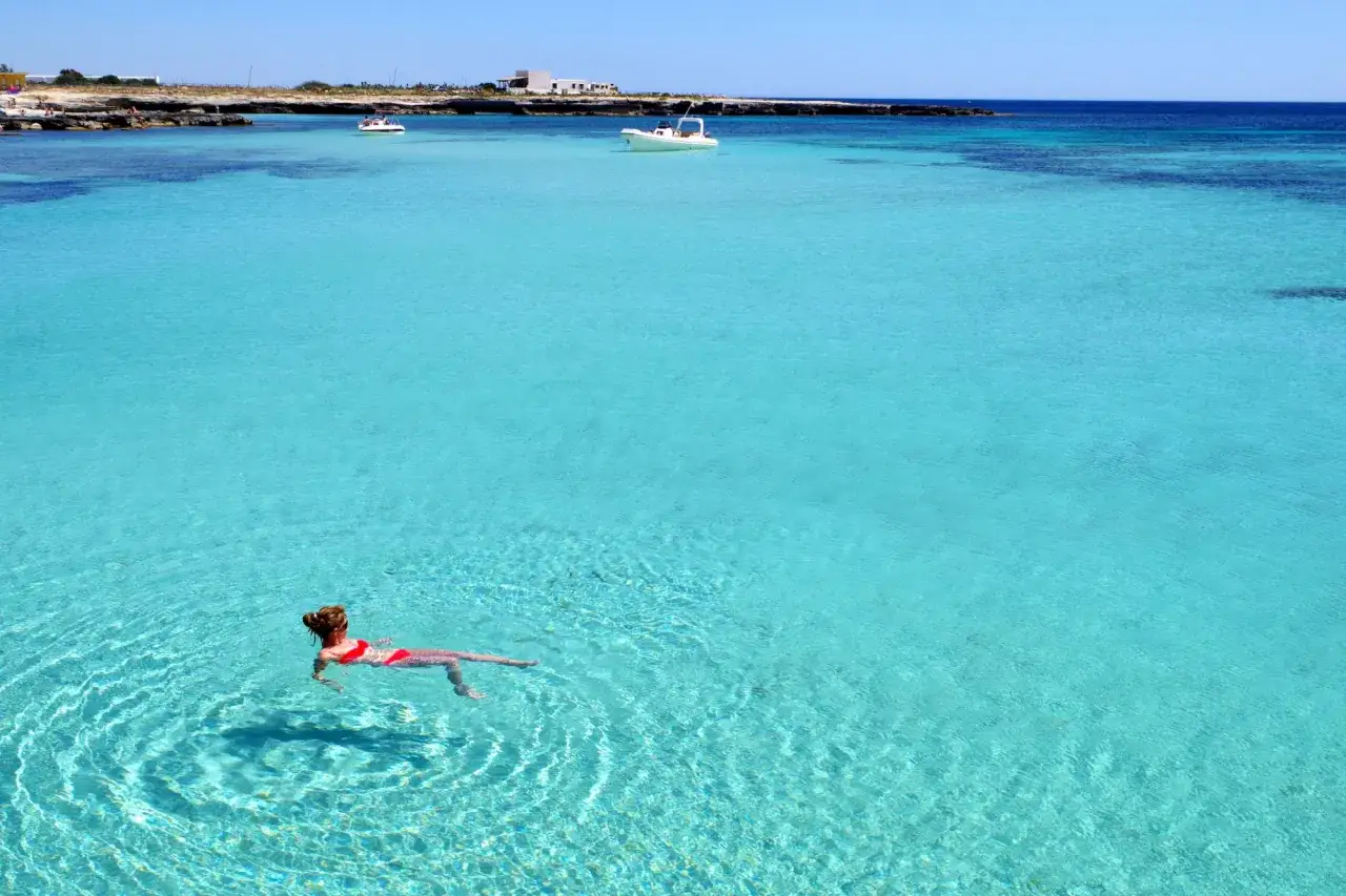 Donna galleggia nell'acqua cristallina, un sogno in quella che sembra la spiaggia più bella di Favignana.
