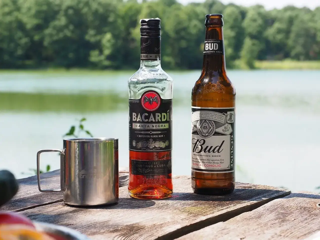 Butelka rumu Bacardi i piwo Bud na drewnianym stole nad jeziorem. Czy wódka może się zepsuć? Termin przydatności do spożycia alkoholi jest długi.