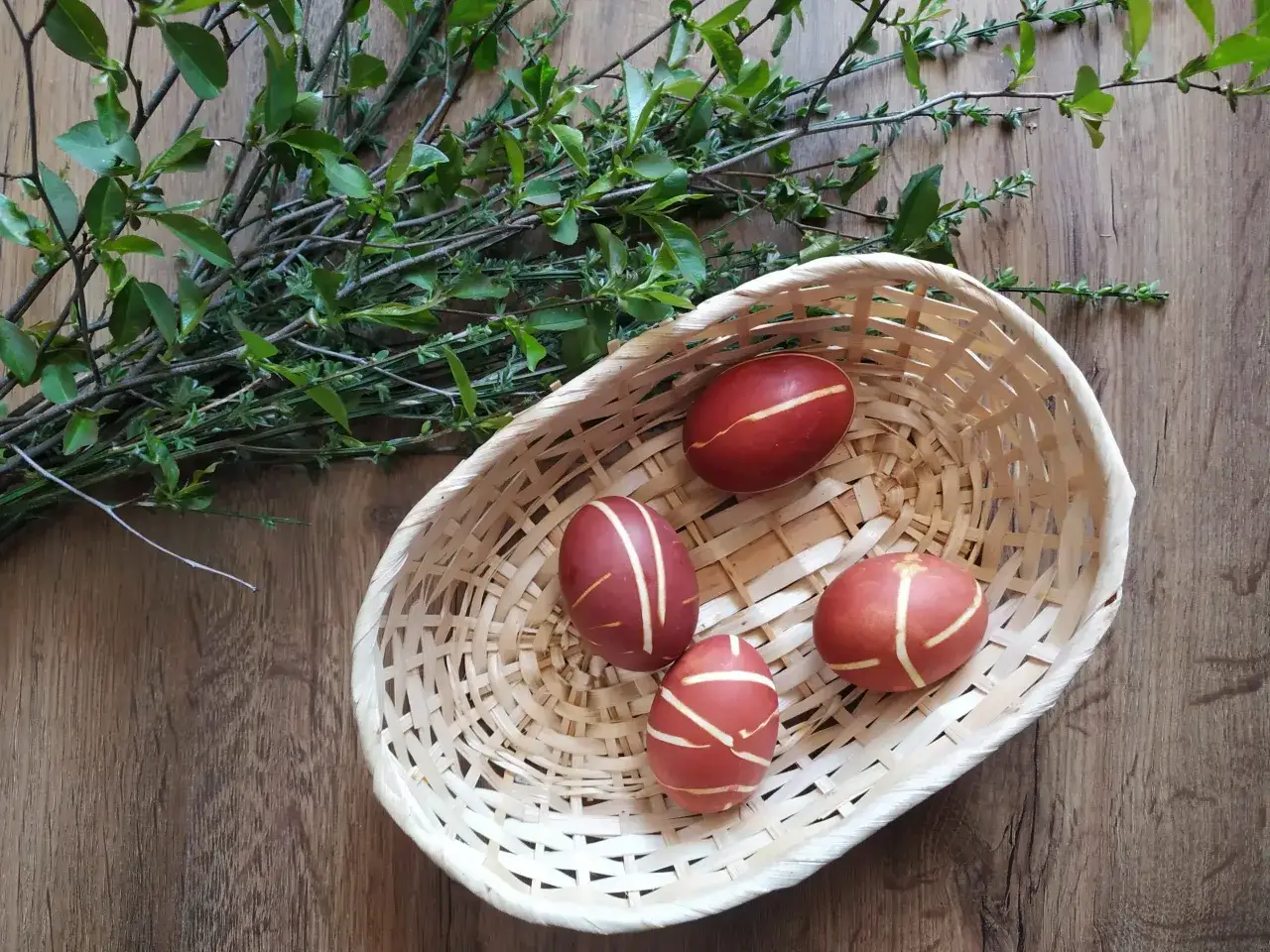Koszyk z pisankami zdobionymi naturalnymi wzorami, obok gałązki z zielonymi listkami. Świetny pomysł na pisanki dla dzieci!