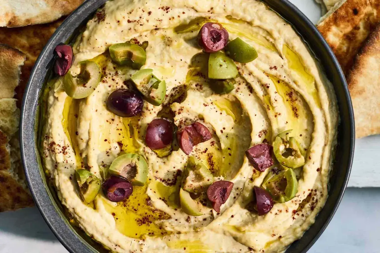 Kremowy hummus z oliwkami i oliwą, posypany przyprawami. Idealny do pieczywa, a jego hummus kcal jest zaskakująco niski.