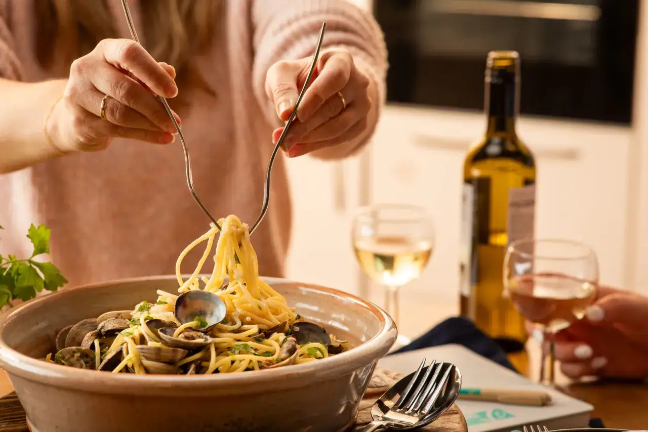 H&auml;nde wickeln Spaghetti Vongole auf, dazu ein Glas Wei&szlig;wein.