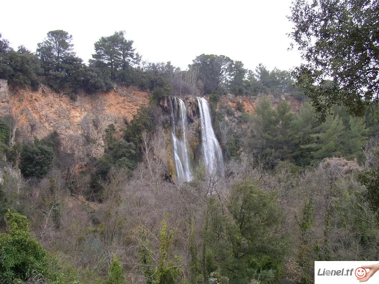 Magnifique cascade près de Gréoux-les-Bains, tombant d'une falaise ocre, entourée d'une végétation dense et d'arbres dénudés.