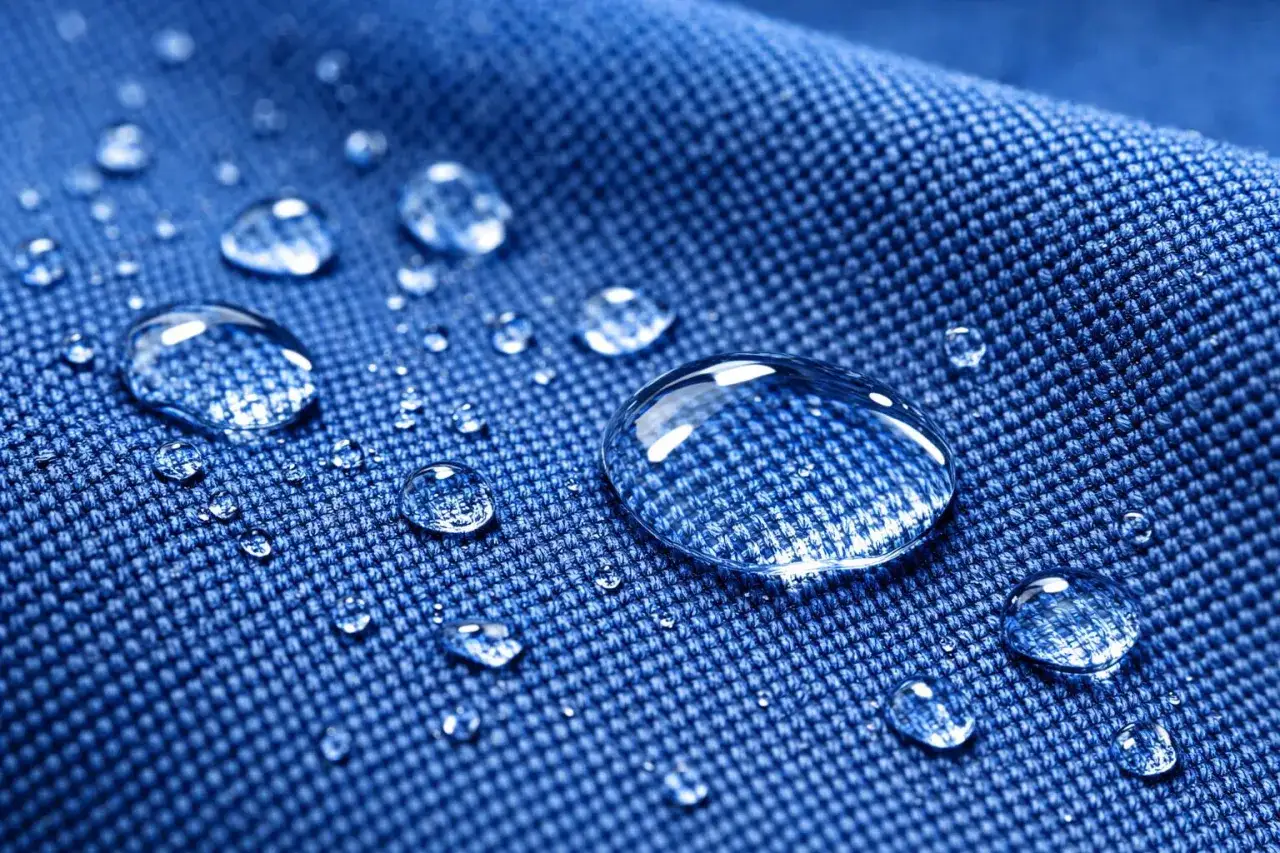 Gouttes d'eau perlant sur un tissu bleu, démontrant ses propriétés de matériaux résistant au chlore.