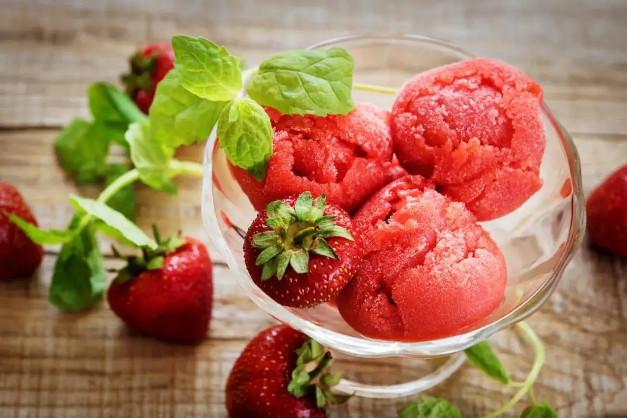 Jak zrobić sorbet truskawkowy? Pyszny, mrożony deser z truskawek i mięty w szklanej miseczce.