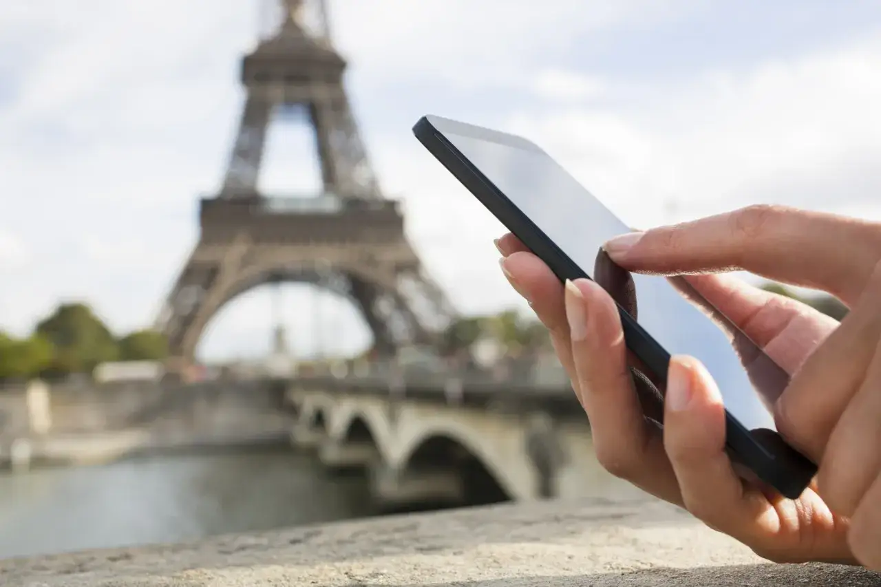 Dłoń trzyma smartfon z widokiem na Wieżę Eiffla. Internet roaming w Paryżu ułatwia dzielenie się wrażeniami.