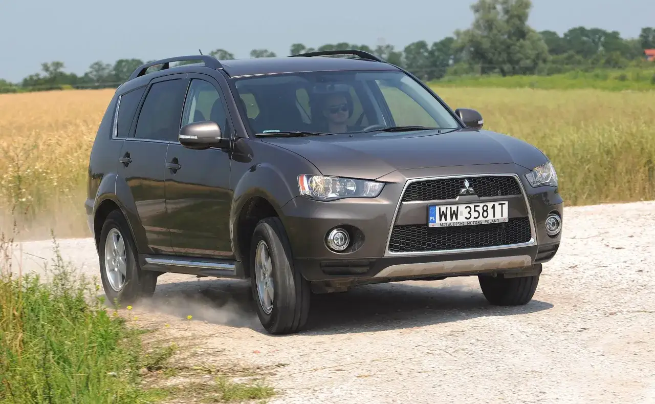 Brązowy Mitsubishi Outlander na drodze polnej, kierowca w okularach. Wiele pozytywnych mitsubishi outlander opinie potwierdza jego wszechstronność.