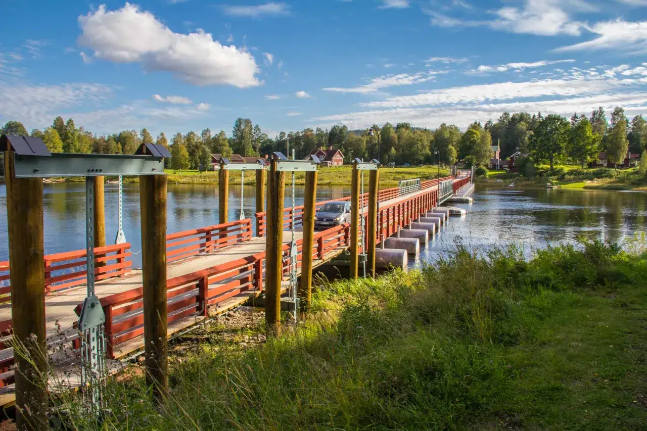 En bil kör över flottbron i Gagnef, en vacker sommardag med blå himmel och vita moln.