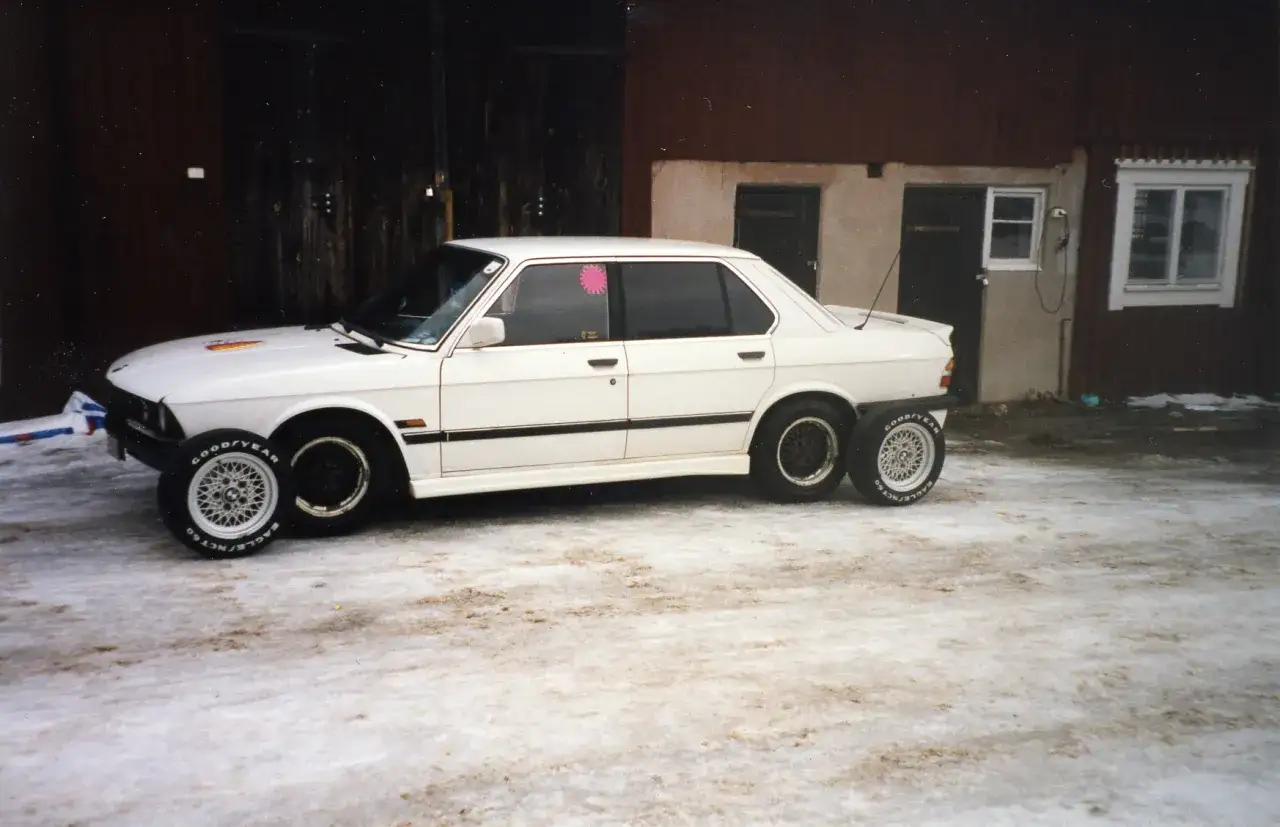 Vit gds bil med dubbla hjul bak och fram, parkerad på snöig mark.