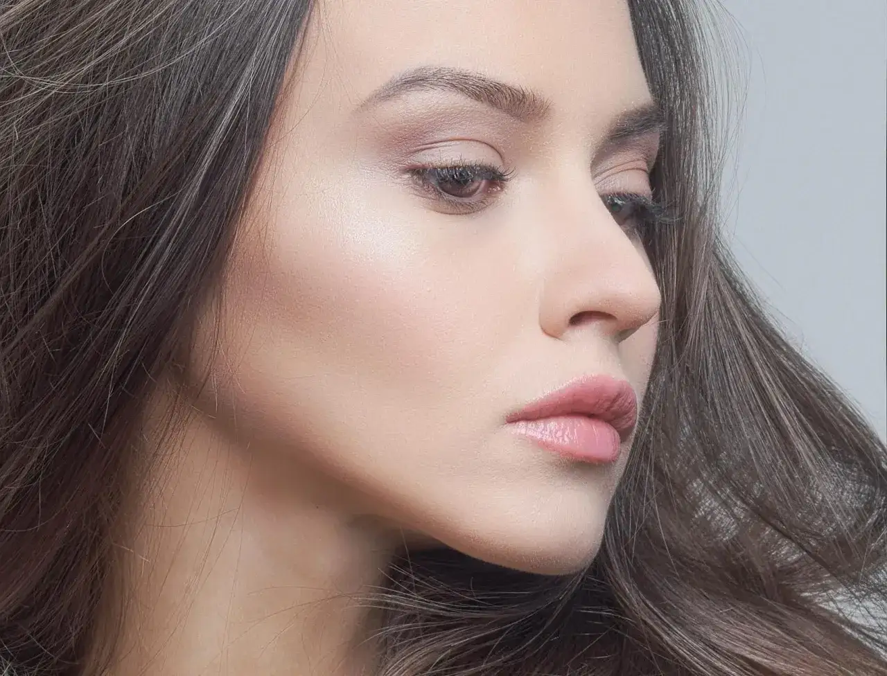 Delikatny, naturalny makijaż typu clean girl podkreśla urodę kobiety. Jasna cera, subtelne cienie na powiekach i błyszczące usta.