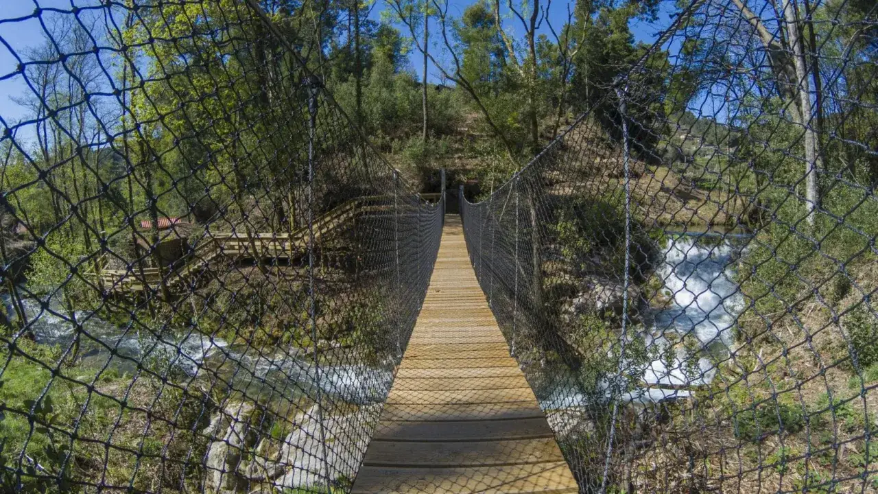 Puente colgante de madera sobre un río caudaloso, ideal para explorar qué ver en Portugal con niños y disfrutar de la naturaleza.