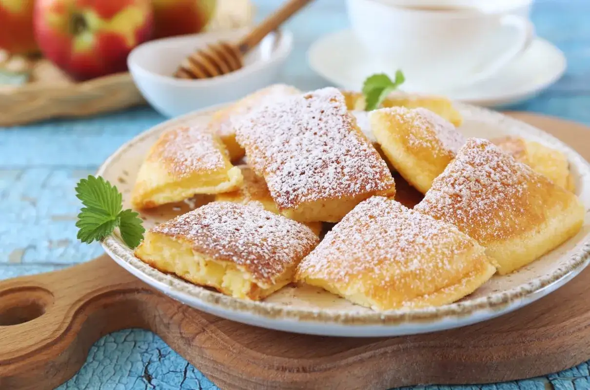 Puszysty omlet z jabłkiem, posypany cukrem pudrem, na talerzu z listkiem mięty. W tle jabłka i filiżanka kawy.