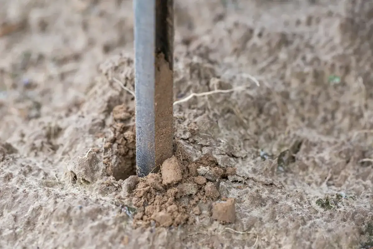 Metalowy pręt wbity w ziemię, tworząc uziom szpilkowy. Wokół rozsypana gleba.