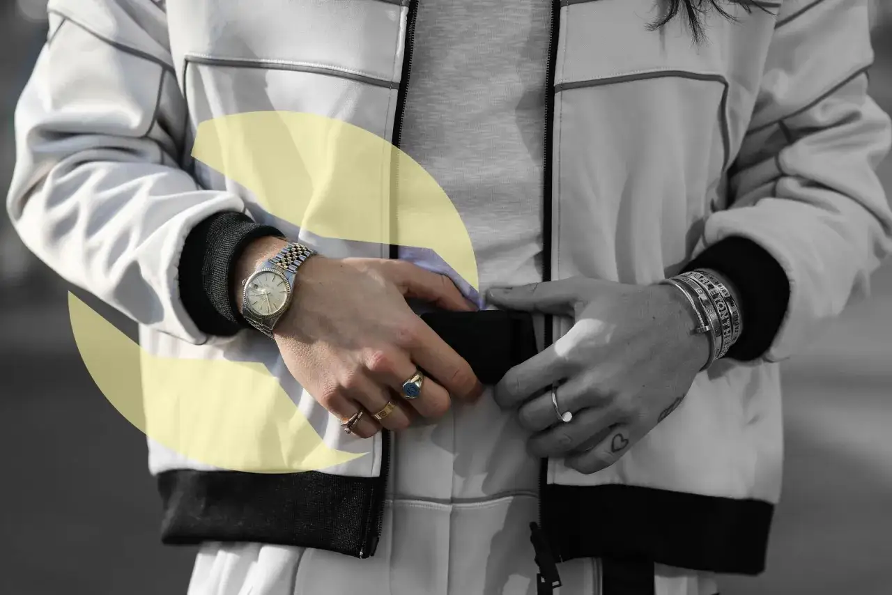 Detalle de un hombre ajustando su chaqueta, luciendo un reloj y varias combinaciones de pulseras en su muñeca.