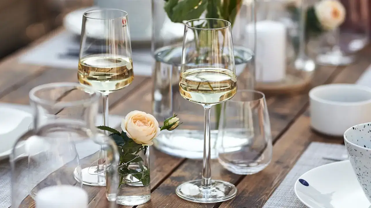 Vackert dukat bord med vinglas fyllda med vitt vin. En liten ros i en vas ger en fin touch. Perfekt för att fundera på hur mycket vin per person som går åt.