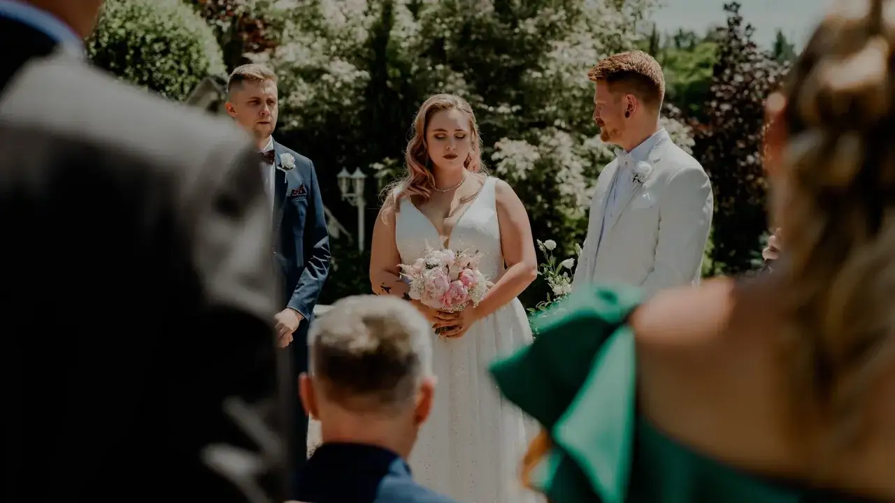Para młoda podczas ceremonii. W tle zieleń, przed nimi goście. To piękny przykład, co to ślub humanistyczny.