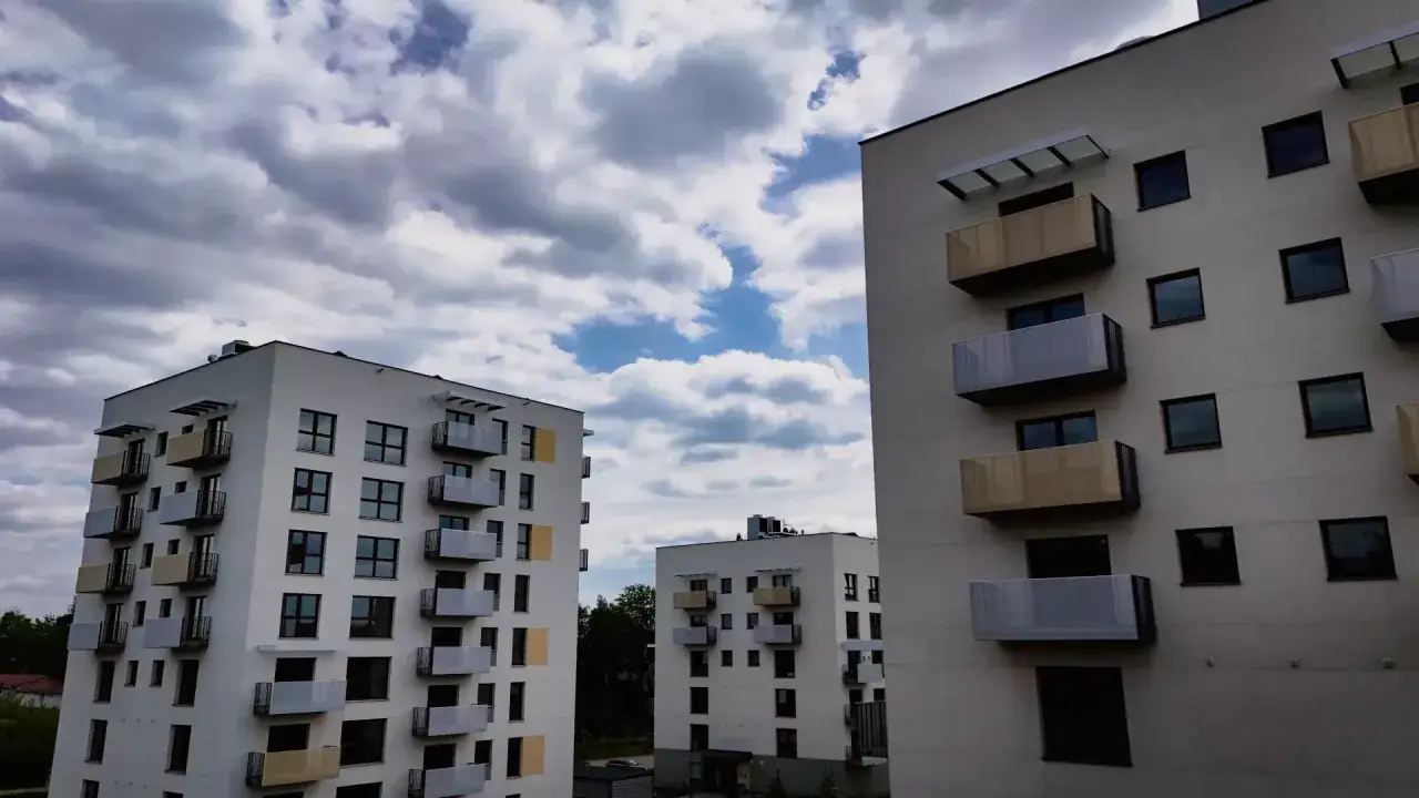 Nowoczesne bloki mieszkalne, idealne na mieszkanie TBS, z balkonami i dużymi oknami, na tle błękitnego nieba z chmurami.