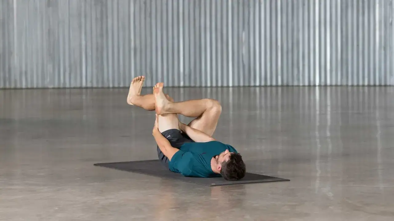 Homme effectuant un étirement piriforme sur un tapis de yoga, jambes croisées, pour soulager les tensions.